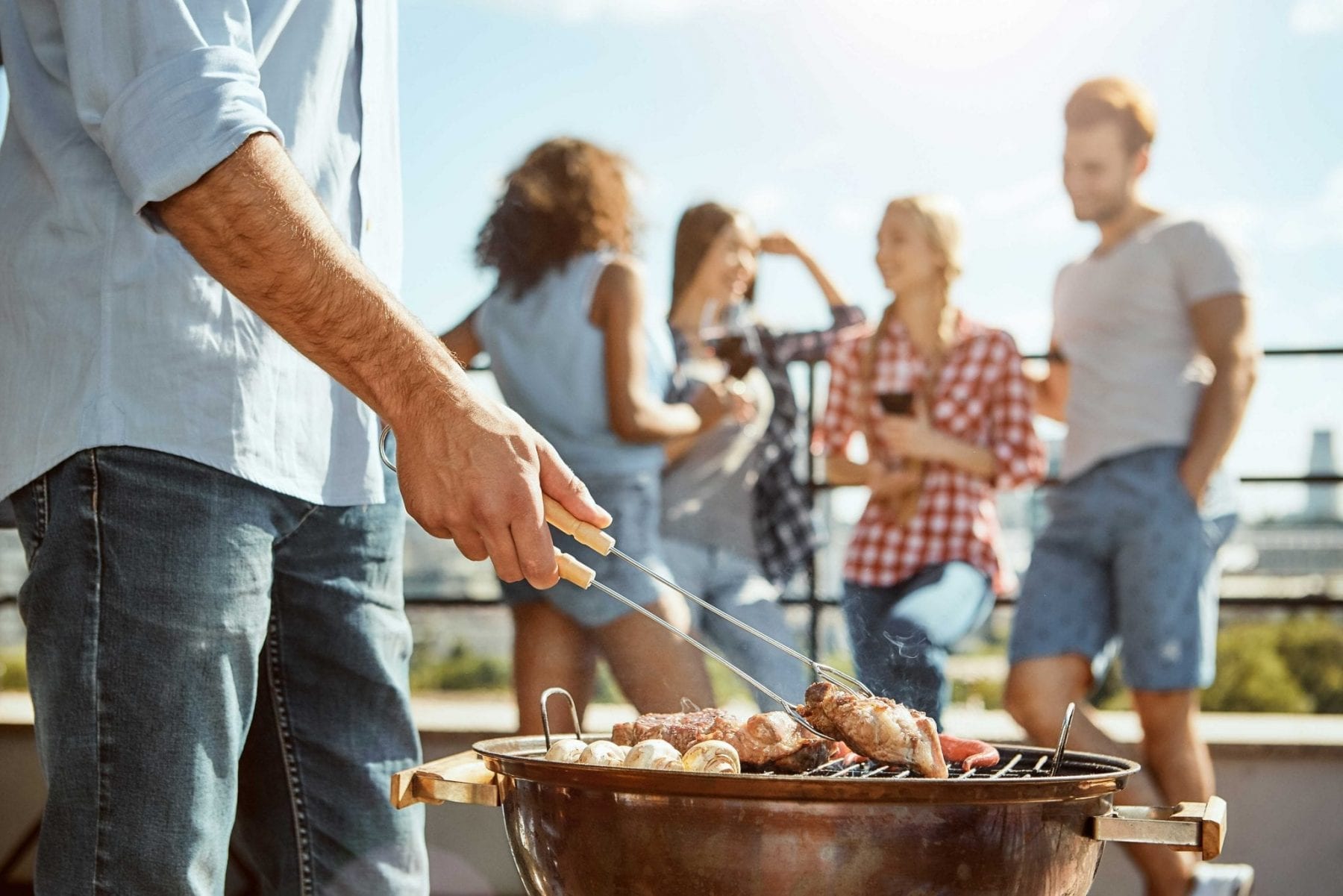 Man grilling outdoors with friends in background