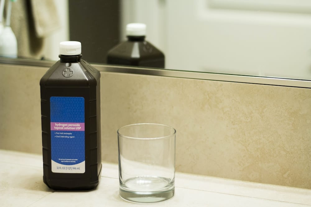 A container of hydrogen peroxide sits next to a glass on a counter.