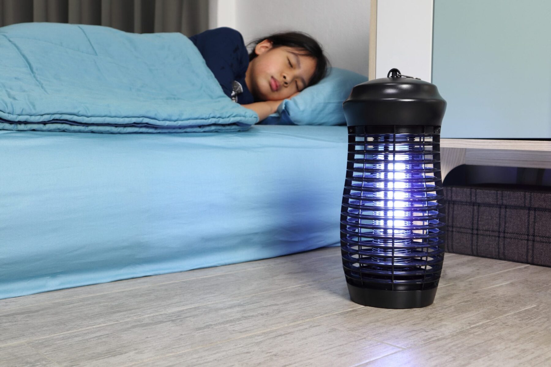 Child sleeping on mattress with blue sheets and bug zapper on the floor next to her