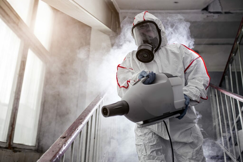 Exterminator in protective suit and mask holding machine to spray for bugs