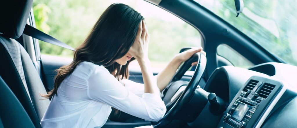 Woman in driver's seat leaning forward with hand up to face