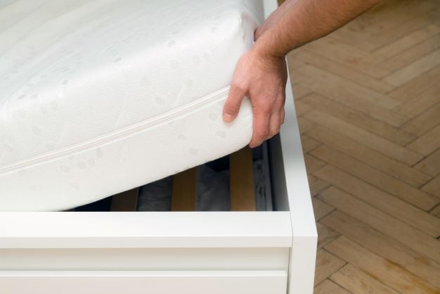Man lifting up mattress out of bed frame for inspection