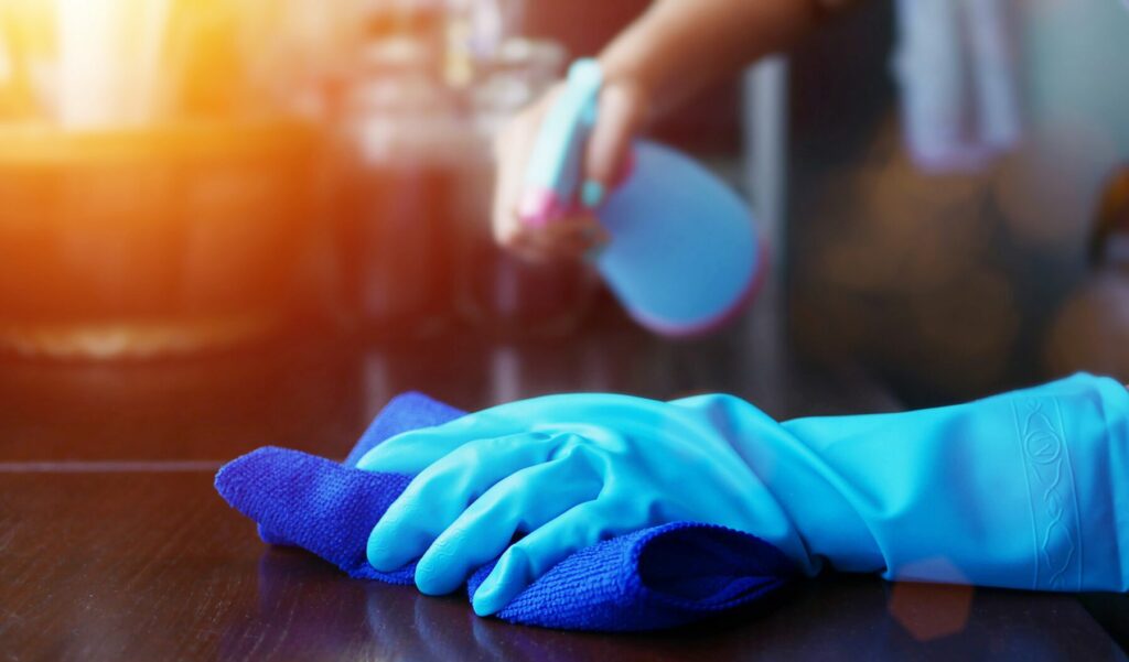 Hand in blue rubber glove holding blue microfiber cleaning cloth and spray bottle
