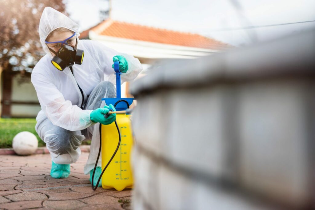 Exterminator in work wear outdoors spraying pesticide with sprayer