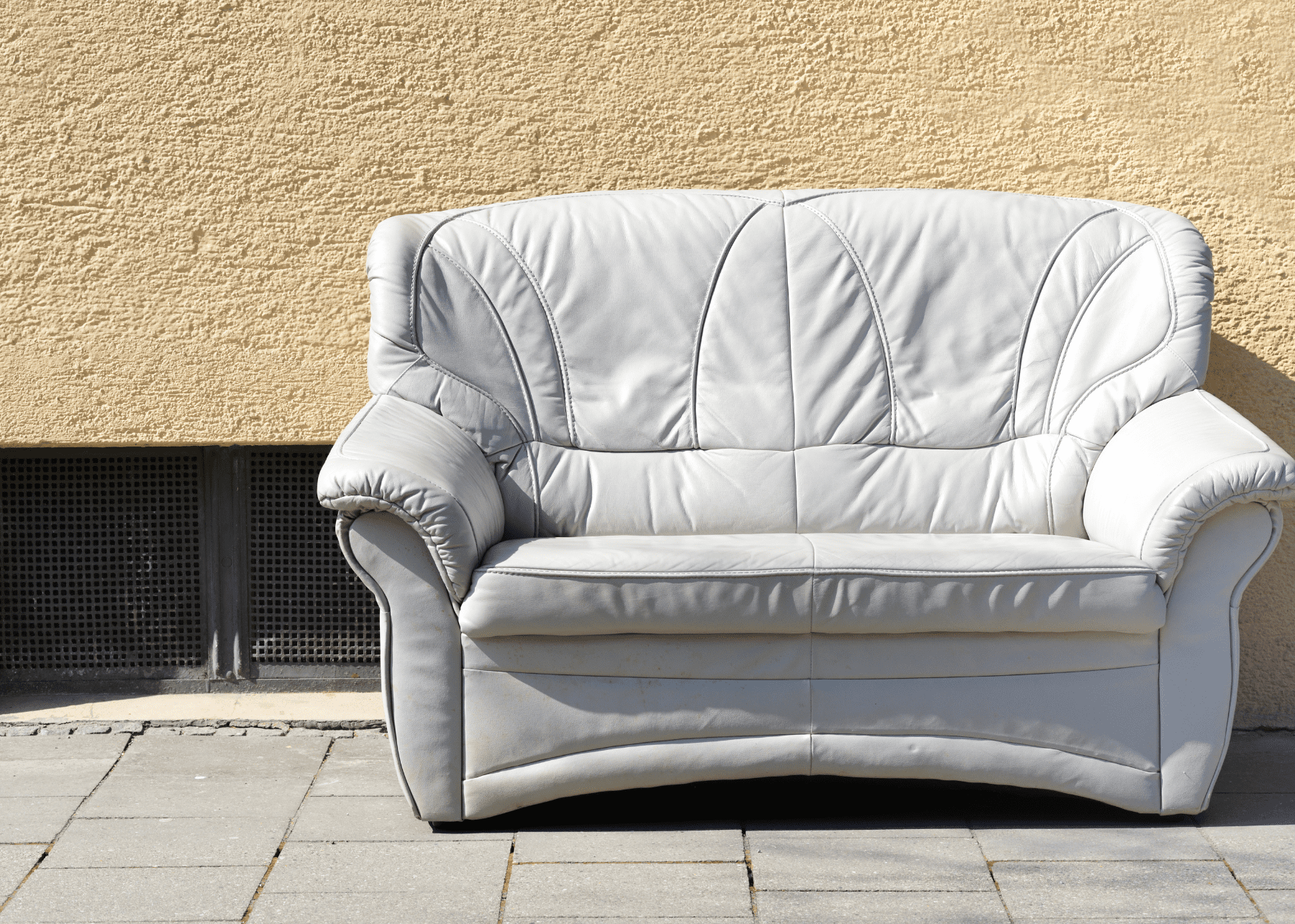 White leather couch on the side of the road against wall of building
