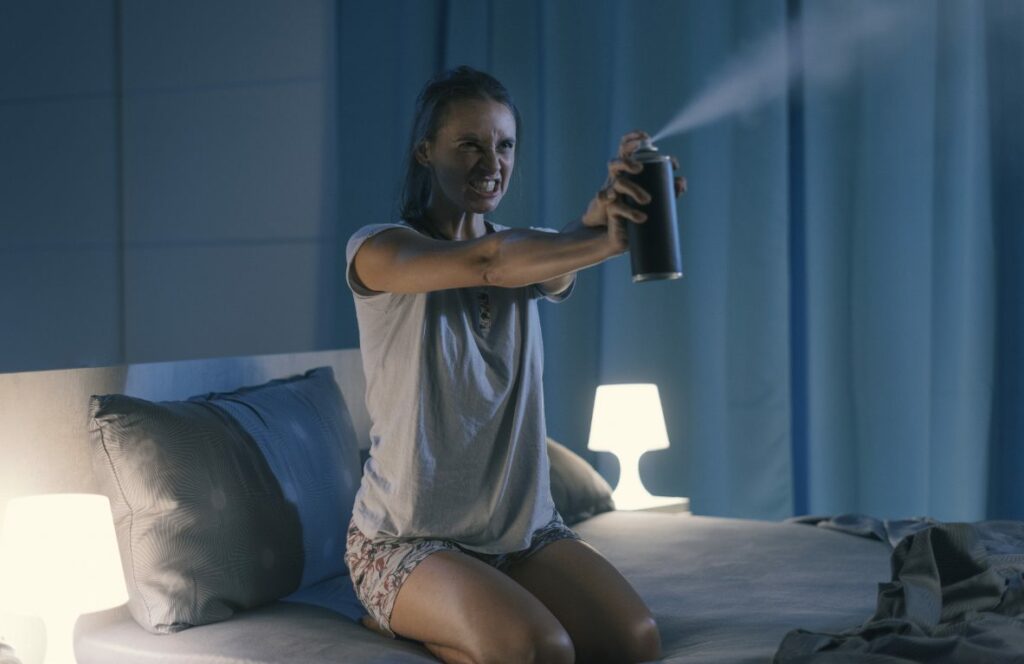 A woman angrily sitting upright in her bed spraying an aerosol can out into the air