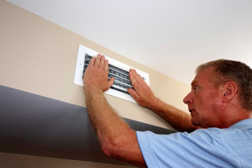 A man in a blue shirt readjusts the cover of an HVAC vent on a wall