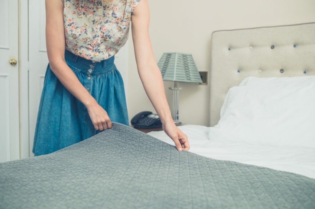 a woman in a floral top and long blue skirt makes her bed.