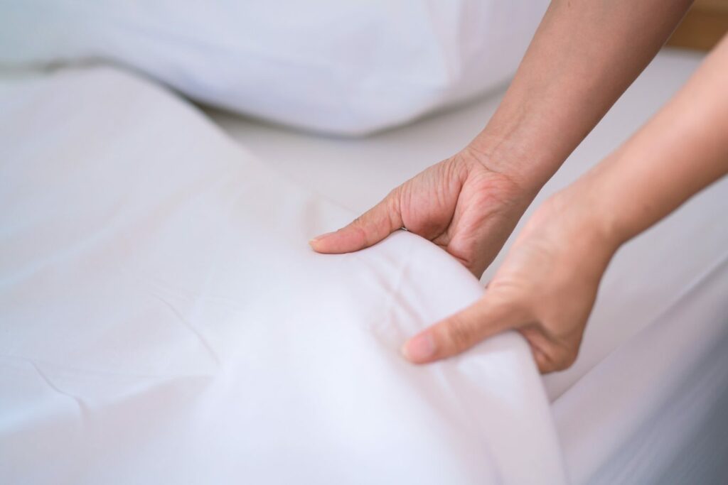 A person pulls a white bedsheet up on a bed