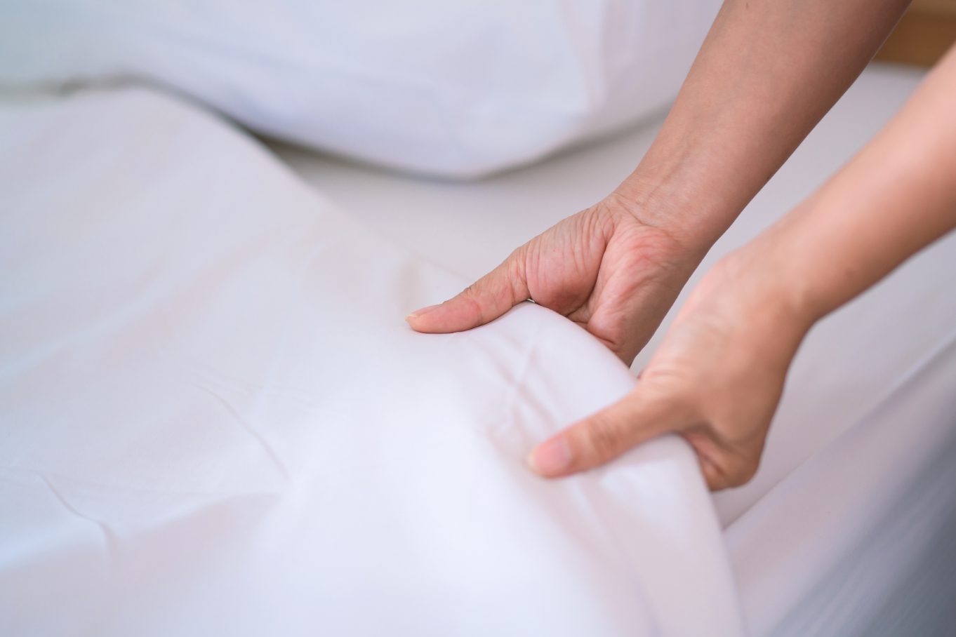 A person pulls a white bedsheet up on a bed